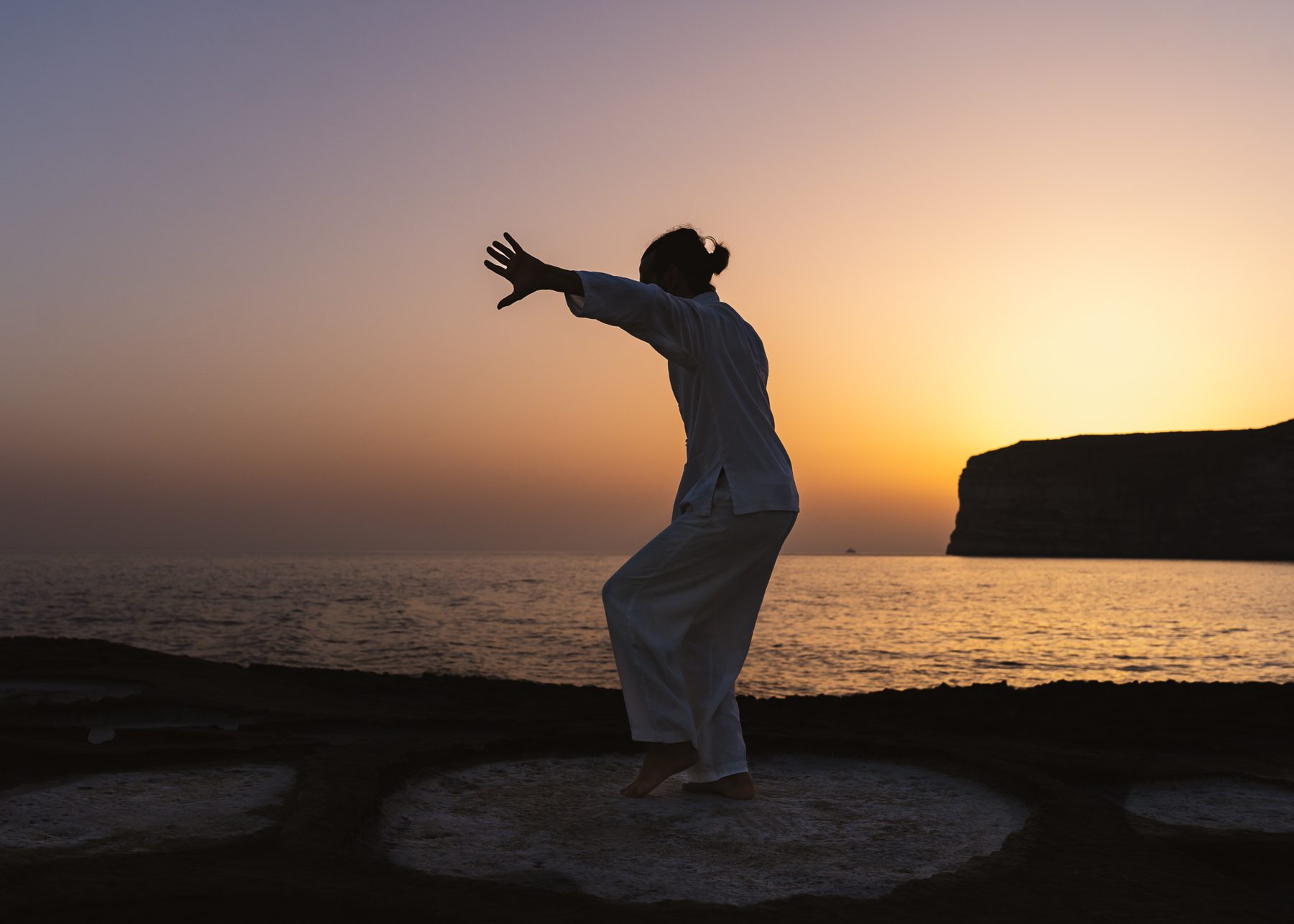 Silhouette doing tai chi by the sea at sunset on Gozo